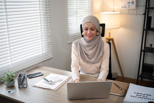 Азиатская мусульманская предпринимательница в хиджабе головной платок, работающая с бумажными документами в современном офисе. разнообразие и концепция офиса. - Фото, изображение