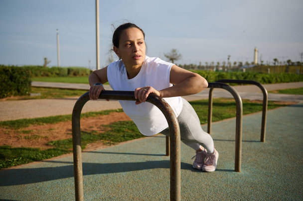Fiatal sportoló nő, aki fitnessz és nyújtózkodik egy sportpályán a városban. Fitness nő gyakorolja push-up a parkban a városi sportpályán. Aktív emberek. Fitness. Egészséges életmód - Fotó, kép