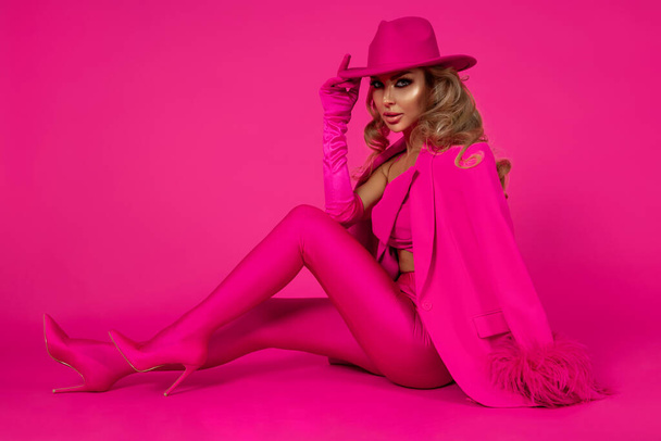 Glamour vrouwelijk model draagt een elegant fuchsia pak, roze laarzen en een roze muts en poseert tegen een roze achtergrond. Monochrome foto in levendige kleur. - Foto, afbeelding