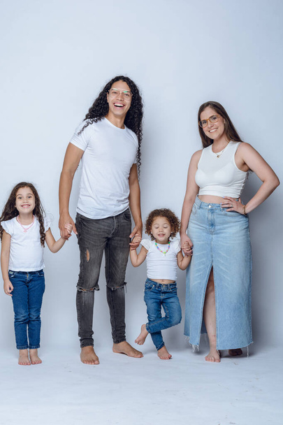 young latin family of father mother and two young girls daughters, having fun posing and smiling, with pants and white flannel, studio shot, white background. - Photo, image