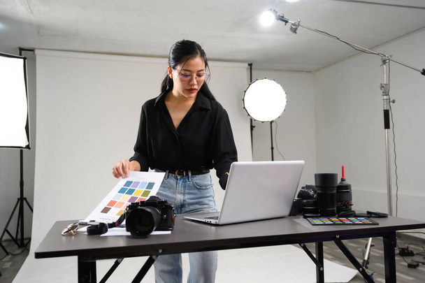 Piękny młody fotograf za pomocą laptopa w nowoczesnym studio fotograficznym. - Zdjęcie, obraz