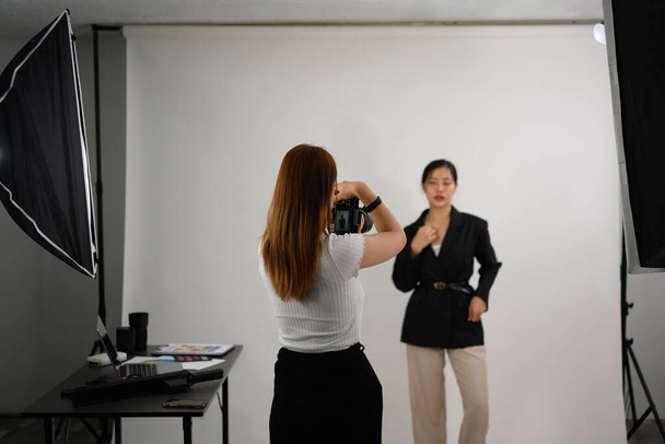 Модний фотограф фотографує жіночу модель з цифровою камерою в освітлювальній студії. - Фото, зображення