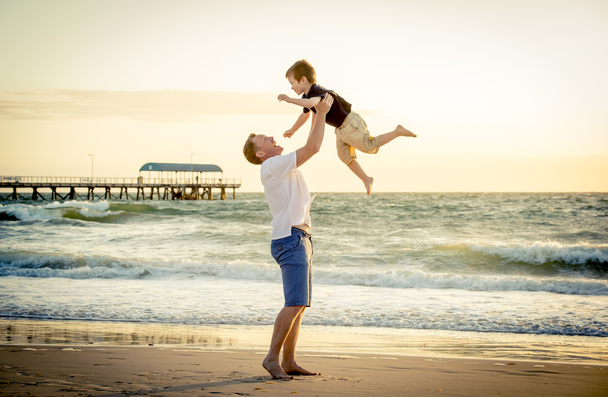 Joven padre feliz sosteniendo en sus brazos pequeño hijo ponerlo en la playa
 - Foto, Imagen