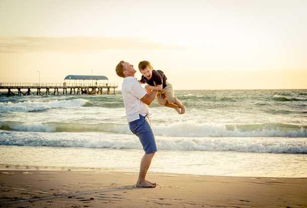 Joven padre feliz sosteniendo en sus brazos pequeño hijo ponerlo en la playa
 - Foto, imagen
