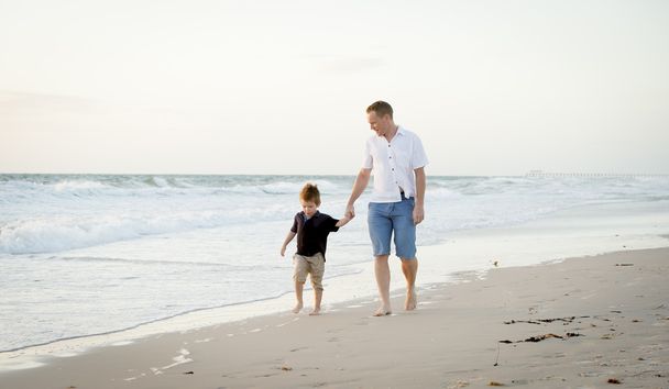 happy father holding holding hand of little son walking together on the beach with barefoot - Photo, Image