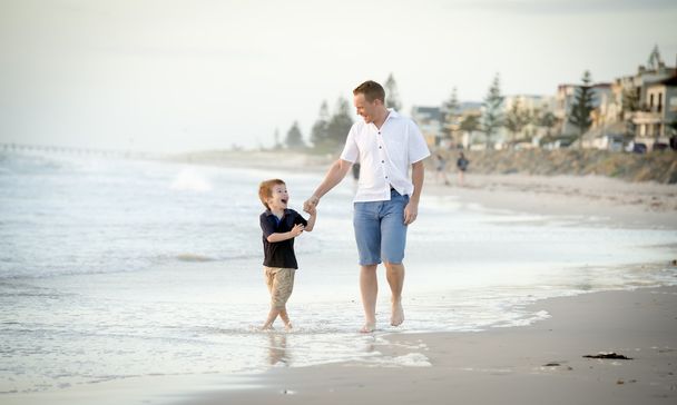 happy father holding holding hand of little son walking together on the beach with barefoot - Photo, Image