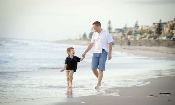 feliz padre sosteniendo de la mano del pequeño hijo caminando juntos en la playa con descalzo
 - Foto, imagen