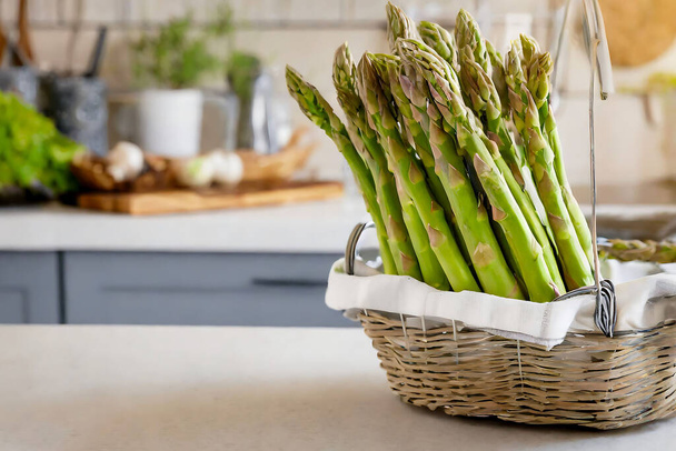 Uma cesta cheia de espargos verdes fica em um balcão de cozinha com fundo embaçado, destacando a alimentação saudável e a culinária em casa. - Foto, Imagem