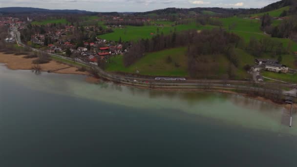 Vonatozás a Tegernsee-tó mentén Bajorország felső részén, Németország légi kilátásban. Drone kilátás a vasúti pálya mentén gyönyörű bajor tó. A vasúti közlekedés témája Németországban. Eisenbahn und See megye.  - Felvétel, videó