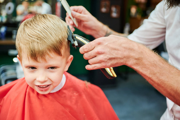 毛を切るのに櫛およびシェーバーを使用する棒. 小さい子供のナイプを剃る専門の美容師. - 写真・画像
