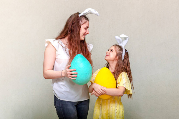 Vrolijk Pasen. Twee meisjes met paashaas oren kijken elkaar aan en houden paaseieren in hun handen. Kopieerruimte. - Foto, afbeelding