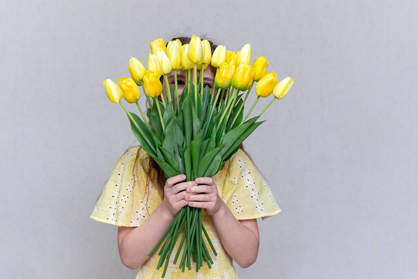 Un ramo de tulipanes amarillos cubre la cara de las chicas. Sin cara. Copiar espacio. - Foto, Imagen