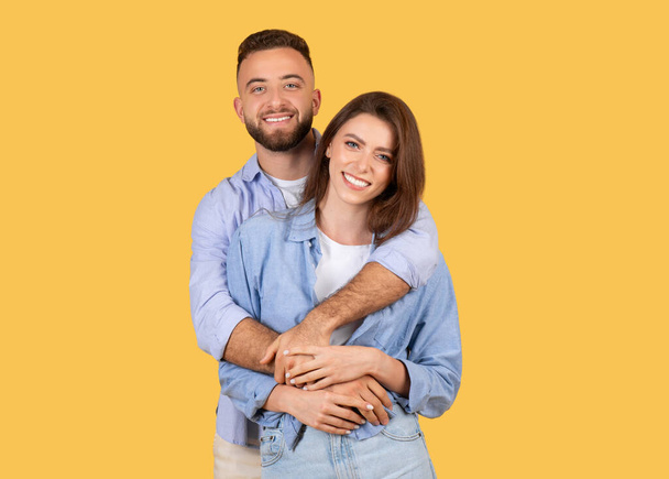 Un couple joyeux s'embrassant avec un bonheur visible, portant des chemises décontractées bleues sur un fond jaune - Photo, image