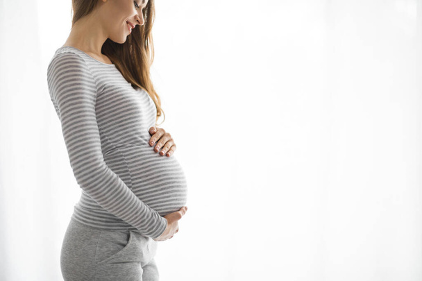 Egy várandós anya hasát gyengéden tartó profilképe jelenti a kapcsolatot a meg nem született gyermekével. - Fotó, kép