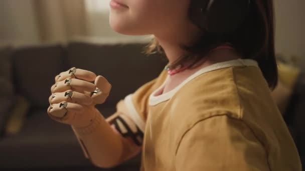 Tilt zbliżenie słodkie biały nastolatek dziewczyna z protezy ramię taniec podczas słuchania muzyki w słuchawki w domu - Materiał filmowy, wideo