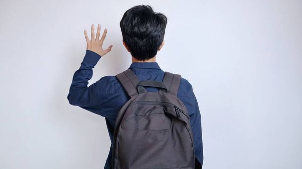 Achteraanzicht van een jonge Aziatische mannelijke student met een tas op een geïsoleerde witte achtergrond - Foto, afbeelding
