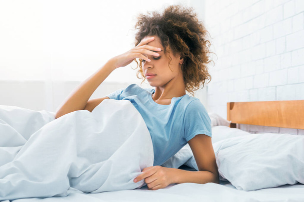 Femme touchant le front, ayant mal à la tête le matin, assise sur le lit
 - Photo, image