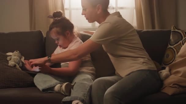 Imágenes laterales de la madre sentada con síndrome de Down hija que usa tableta digital y ve dibujos animados en casa - Metraje, vídeo