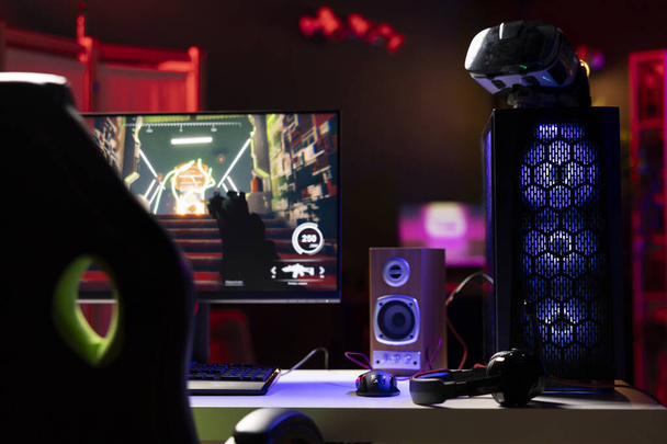 Estudio de sala vacía para juegos profesionales con luces de neón y computadora iluminada RGB junto a auriculares y auriculares VR. Videojuego FPS en pantalla de PC y gafas de realidad virtual en apartamento - Foto, Imagen