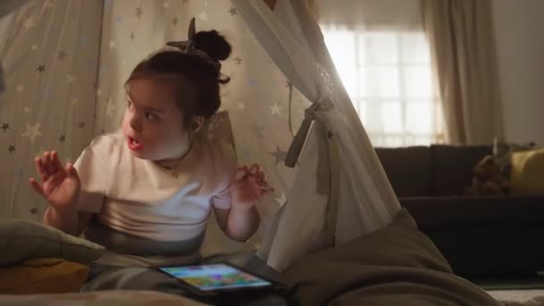 Kompletní záběry šťastného bělocha dolů syndrom dívka sedí uvnitř zdobené teepee, tleskání rukou a pak sledovat karikatury na digitálním tabletu - Záběry, video