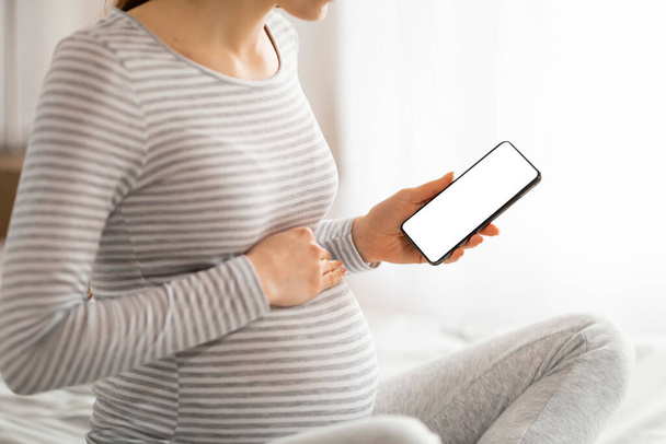 Klares Bild einer Schwangeren, die einen leeren Smartphone-Bildschirm zeigt, der für Werbung oder App-Demonstrationen geeignet ist - Foto, Bild