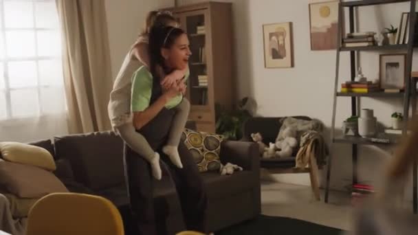 Side footage of active happy mom giving her daughter with disability piggyback ride and turning around in living room with granny dancing and feeling excited - Materiał filmowy, wideo