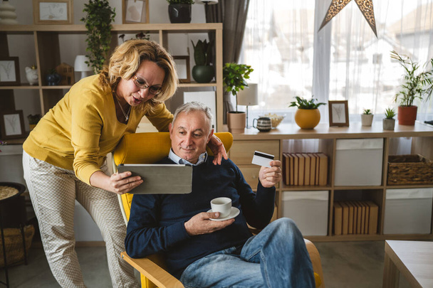 Couple mature homme caucasien senior et femme mari et femme à la maison shopping en ligne e-banking détenir carte de crédit ou de débit - Photo, image