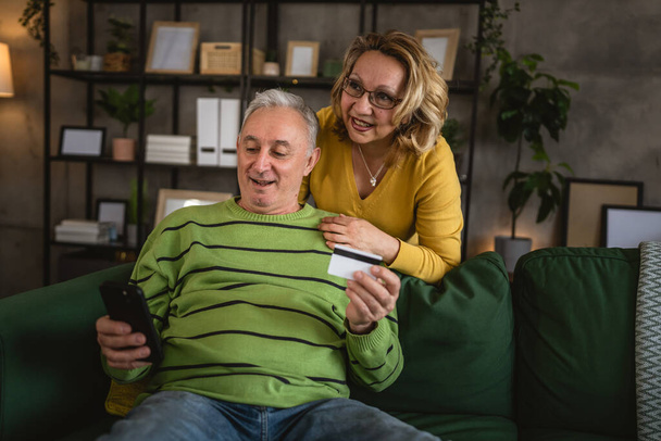 Pár starší starší kavkazský muž a žena manžel a manželka doma nakupování on-line e-banking držet kreditní nebo debetní karty - Fotografie, Obrázek
