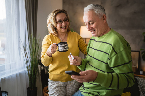 Couple mature senior caucasian man and woman husband and wife at home shopping online e-banking hold credit or debit card - Photo, Image