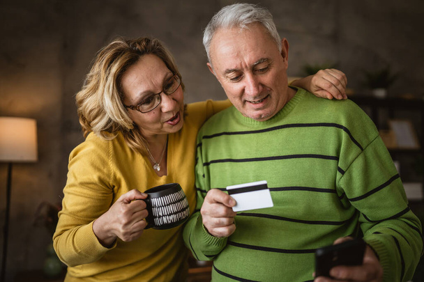 Couple mature senior caucasian man and woman husband and wife at home shopping online e-banking hold credit or debit card - Photo, Image