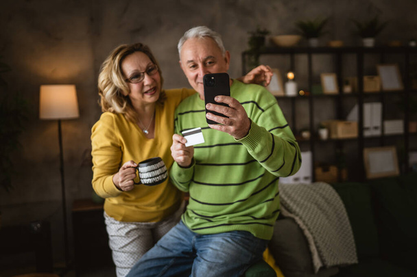 Пара зрілих старший кавказький чоловік і жінка чоловік і дружина вдома покупки онлайн електронного банкінгу тримають кредитну або дебетову картку - Фото, зображення