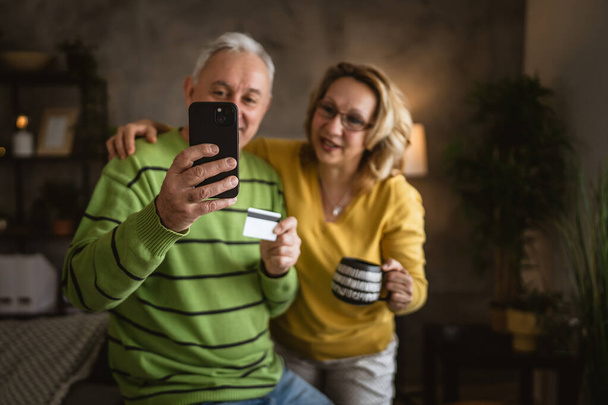 Pár starší starší kavkazský muž a žena manžel a manželka doma nakupování on-line e-banking držet kreditní nebo debetní karty - Fotografie, Obrázek