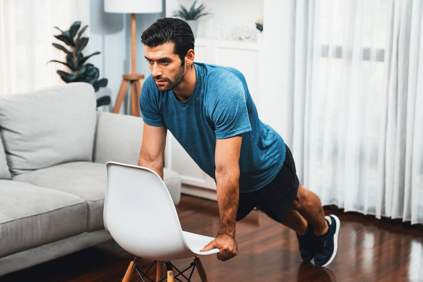 健康的なフィットボディホームワークアウトのライフスタイルのコンセプトとして,効果的なターゲティング筋肉の運動のための家具を使用して運動体とアクティブスポーティーな男性. - 写真・画像