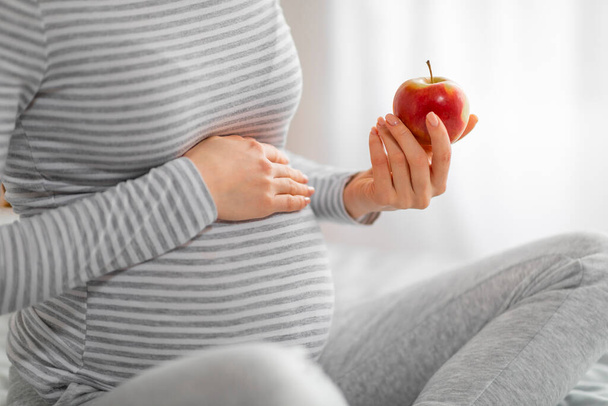 La imagen muestra a una mujer embarazada serena sosteniendo suavemente una manzana roja, lo que significa elecciones nutricionales inteligentes - Foto, Imagen
