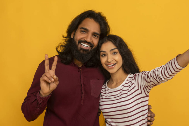 Animated couple taking a selfie with woman flashing a peace sign, both smiling warmly on yellow background - Photo, Image