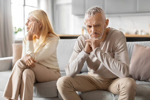 A man is seen comforting a visibly upset woman, while sitting apart on a sofa in a home setting - Photo, Image