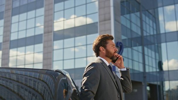 Businessman discussing work by smartphone call leaning on expensive car outdoors close up. Smart bearded manager talking cellphone on street. Confident man ceo speaking partners. Camera moving around. - Photo, Image