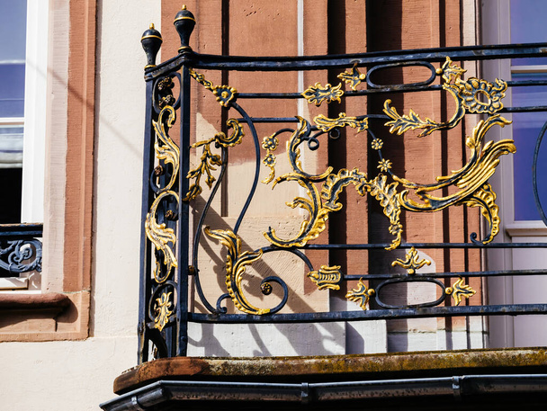 Ένα μπαλκόνι που διαθέτει ένα διακοσμητικό σφυρήλατο κάγκελο με θέα σε ένα παράθυρο με θέα το περιβάλλον. - Φωτογραφία, εικόνα