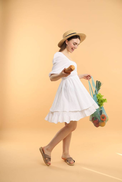 Woman with string bag of fresh vegetables and baguette on beige background - Foto, Imagem