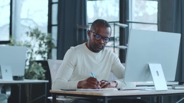 Un hombre está sentado en un escritorio, enfocado en la pantalla de su computadora portátil, escribiendo y trabajando diligentemente. - Metraje, vídeo