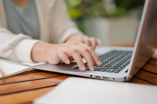 Przycięty obraz kobiety w luźnym ubraniu pracuje zdalnie w przestrzeni zewnętrznej, wpisując na klawiaturze laptopa, pracując lub przeglądając internet na swoim laptopie. - Zdjęcie, obraz