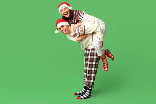 Happy young couple in Christmas pajamas having fun on green background - Photo, Image