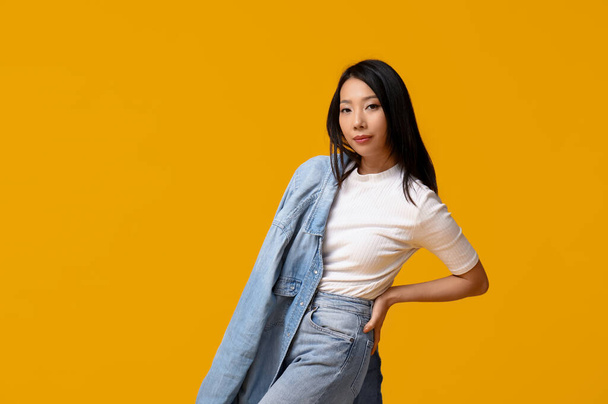 Schöne junge Asiatin in stylischer Jeanskleidung auf gelbem Hintergrund - Foto, Bild