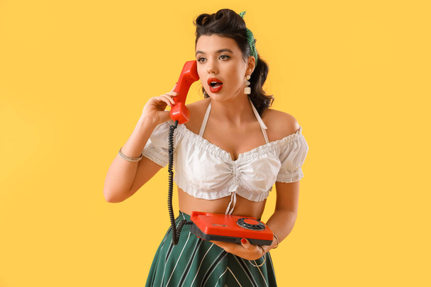 Привлекательная пинап-женщина разговаривает по телефону на желтом фоне - Фото, изображение