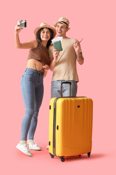 Pareja de turistas con maleta y pasaportes tomando selfie sobre fondo rosa - Foto, Imagen