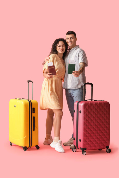 ピンクの背景にパスポートやスーツケースを持つ観光客のカップル - 写真・画像