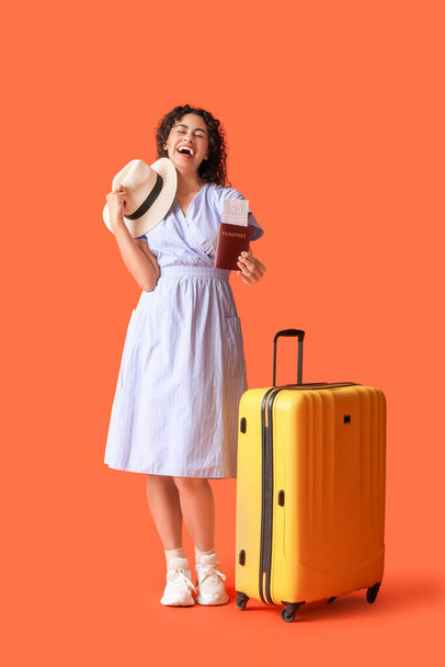 Fiatal afro-amerikai női turista bőrönddel és útlevéllel narancssárga alapon - Fotó, kép