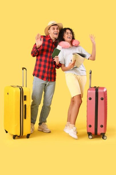 Couple of tourists with suitcases, passport and map waving hands on yellow background - Photo, Image