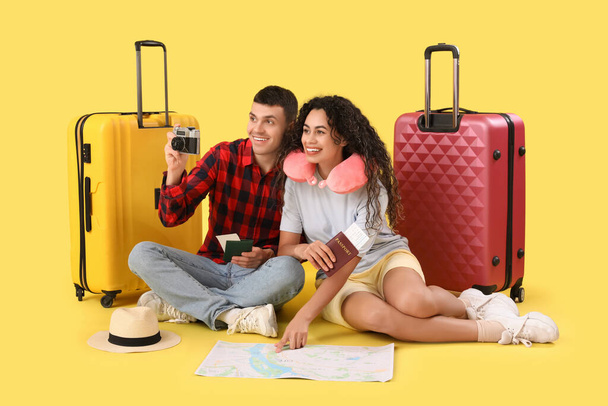 Δύο τουρίστες με βαλίτσες, διαβατήρια και φωτογραφική μηχανή κάθεται σε κίτρινο φόντο - Φωτογραφία, εικόνα