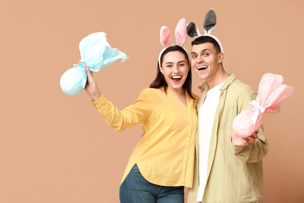 Feliz pareja joven con orejas de conejo de Pascua y regalos sobre fondo beige - Foto, imagen